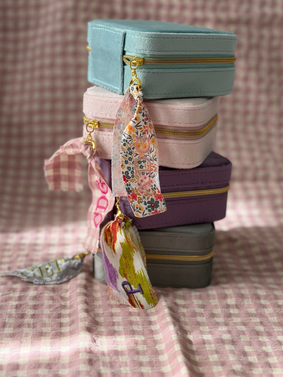 Joyeros de viaje personalizables apilados en cuatro colores: menta, rosa, morado y gris, con cintas personalizadas