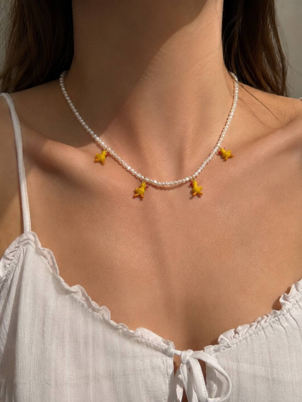Collar de perlas naturales con cuatro charms esmaltados de patitos amarillos y cierre dorado puesto en cuello