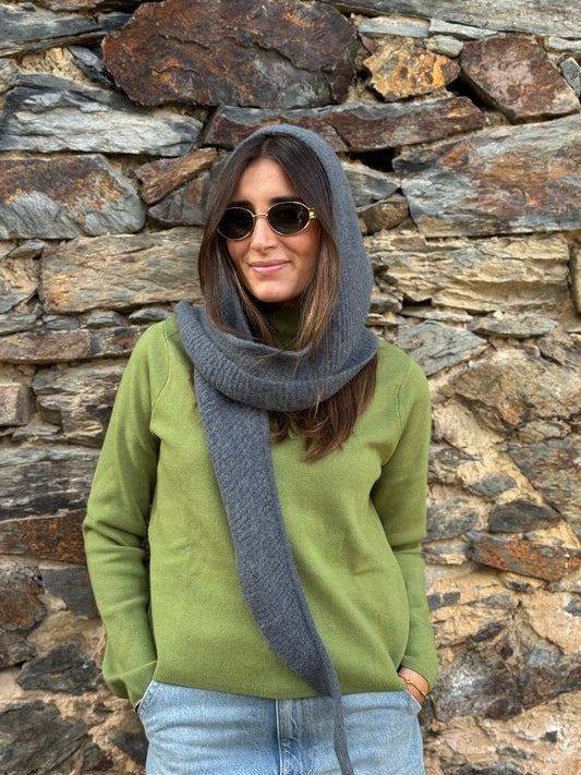 Mujer con capucha de punto gris de lana y alpaca puesta sobre la cabeza, con jersey verde y gafas de sol